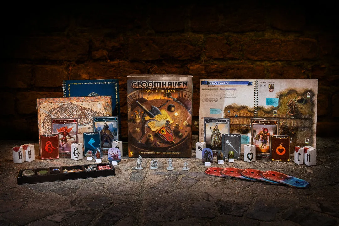 Official spread of Gloomhaven: Jaws of the Lion: the box surrounded by the scenario book, character mats, cards, standees and miniatures