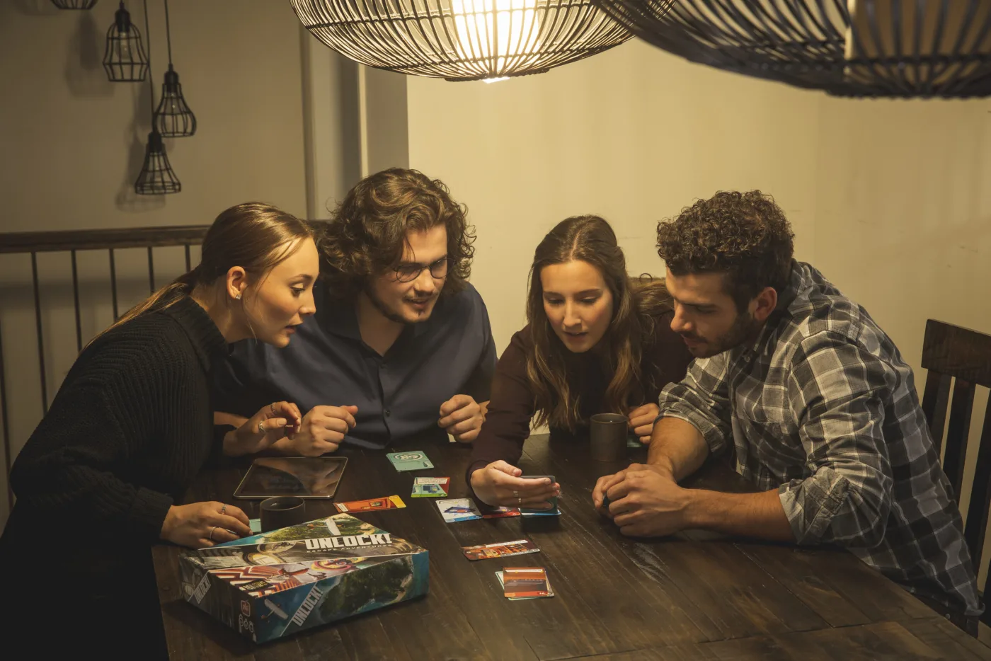 Four players leaning over Unlock! cards, with the box and the companion-app tablet nearby